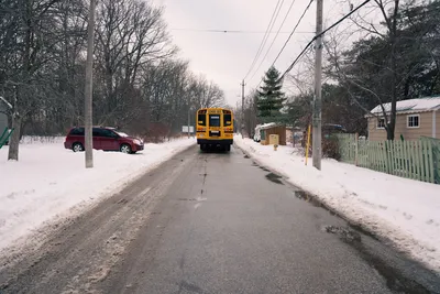 A yellow school bus driving down a snowy suburban street during winter. Captures a typical winter morning commute.