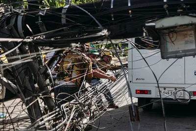Workers managing tangled power lines by a street setup near a vehicle, highlighting infrastructure challenges.